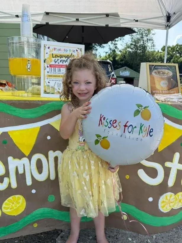 A child at a Kisses for Kyle lemonade stand holding a foundation balloon